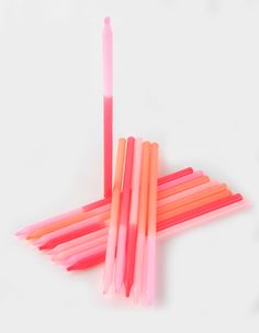 several pink and orange straws are lined up on a white surface, with one yellow stick sticking out from the top