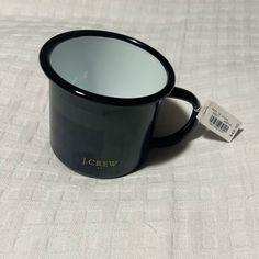 a black coffee mug sitting on top of a white tablecloth with a tag attached to it