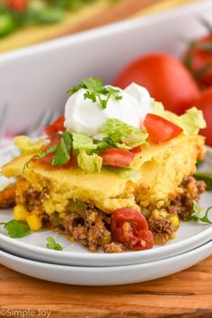 a white plate topped with an enchilada casserole next to tomatoes