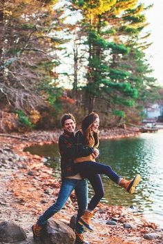 a man and woman standing next to each other in front of a lake