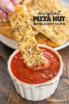 a person dipping pizza hut bread sticks into a bowl of marinara sauce