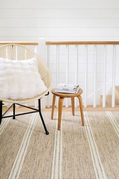 a chair and ottoman in a room with white walls, wood railings and striped rug on the floor