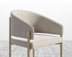 an upholstered chair with a gold frame and beige fabric, in front of a white wall