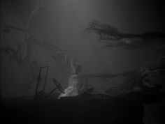 a woman sitting on top of a couch in the middle of a dark room with lots of hair flying over her head