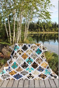 a quilted blanket sitting on top of a wooden deck next to a lake and trees