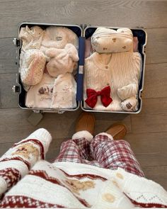 two suitcases filled with baby clothes on top of a wooden floor next to a person's feet