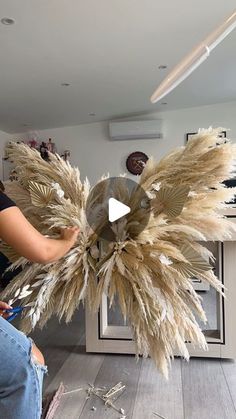 a woman is working on a sculpture made out of dried grass and feathers in a living room