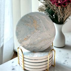 a marble ball sitting on top of three stacked white and gold coasters next to a vase with flowers in it