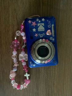 a blue camera sitting on top of a wooden table next to a necklace and bracelet