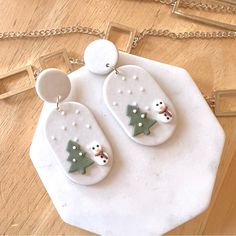 two snowmen are hanging from the back of some white necklaces on a wooden table