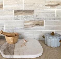 a wooden bowl sitting on top of a cutting board next to a wall covered in tiles