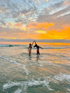 two people are standing in the ocean with their arms around each other as the sun sets