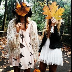 two young women dressed in costumes and holding leaves over their heads while walking down a path