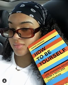 a woman sitting in the back seat of a car holding up a book that says how to be yourself