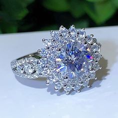 a diamond ring on a white surface with green leaves in the backgrouf