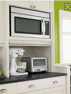 a kitchen with white cabinets and black counter tops, green walls and an open microwave