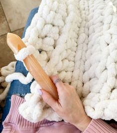 a woman is holding a wooden toothbrush in her hand while she sits on a blanket