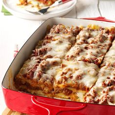 a red casserole dish filled with meat and cheese covered lasagna sauce