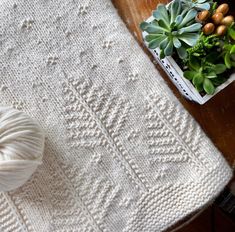 a white knitted blanket sitting on top of a wooden table next to a ball of yarn