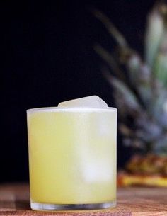 a yellow candle sitting on top of a wooden table next to a pineapple plant