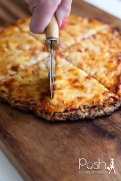 a person cutting into a pizza on top of a wooden cutting board with a knife