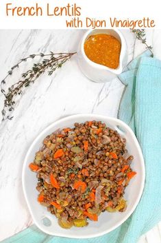 a white bowl filled with lentils and carrots next to a small bowl of dipping sauce