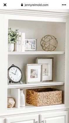 a white bookcase with pictures and other items on it, including an alarm clock