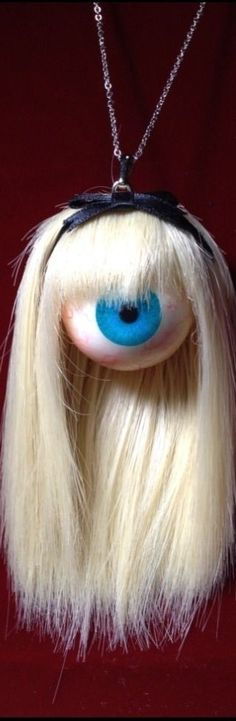 a doll with long blonde hair and blue eyes is hanging from a chain on a red background