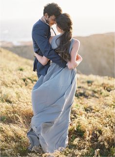 a man and woman standing on top of a grass covered hill next to each other