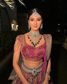 a woman in a pink and green outfit with jewelry on her head, standing outside at night