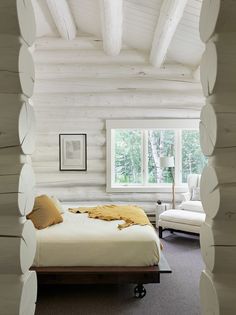 a bed sitting in the middle of a bedroom next to a white chair and window