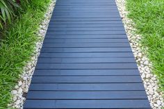 a black wooden walkway surrounded by grass and rocks