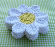 a crocheted white flower with yellow center sitting on a green and white checkered tablecloth