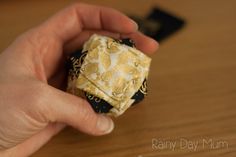 a hand holding a small yellow and black origami object on top of a wooden table