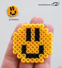 a hand holding a yellow and black beaded brooch with the letter b on it