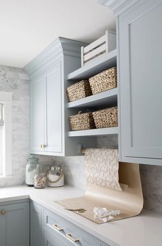 a kitchen with white cabinets and gray counter tops in front of a window that has baskets on it