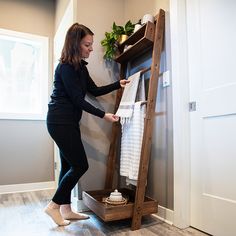 a woman standing next to a wooden ladder holding a white towel on top of it