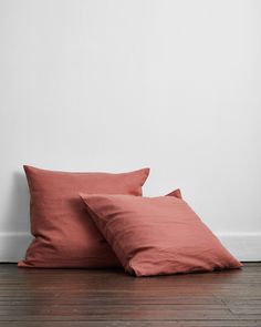 two pink pillows sitting on top of a wooden floor next to a white painted wall