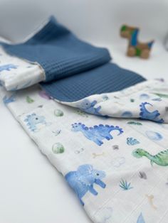 a baby's blanket with blue and white dinosaurs on it, next to toys