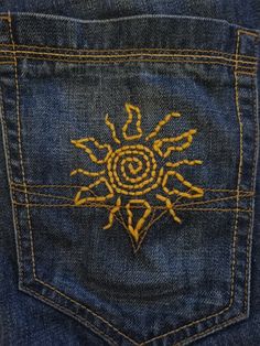 the back pocket of a pair of jeans with an embroidered sun design on one side