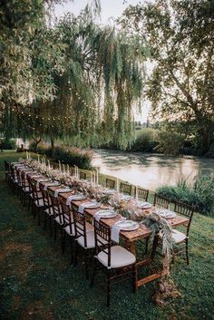 a long table set up for an outdoor dinner by the river