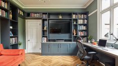 a home office with bookshelves, desk and couch in front of the window