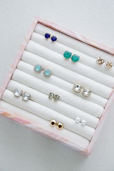 an assortment of earrings in a pink and white jewelry box on top of a table