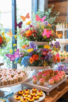 a table topped with lots of cupcakes covered in frosting next to flowers