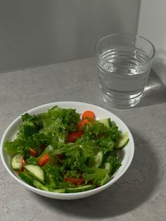 a salad in a white bowl next to a glass of water on a counter top