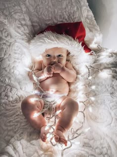 a baby wearing a santa hat laying on top of a bed covered in white blankets