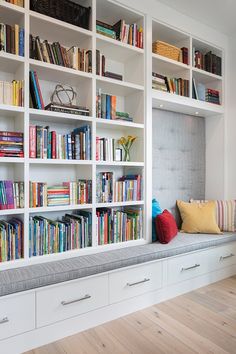 the bookshelves are filled with many different types of books and have colorful pillows on them