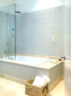 a bath tub sitting next to a walk in shower and a basket with towels on it