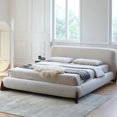 a large white bed sitting on top of a wooden floor next to a tall window