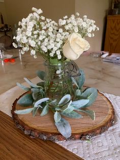 white flowers are in a glass vase on top of a wood slice that is sitting on a table